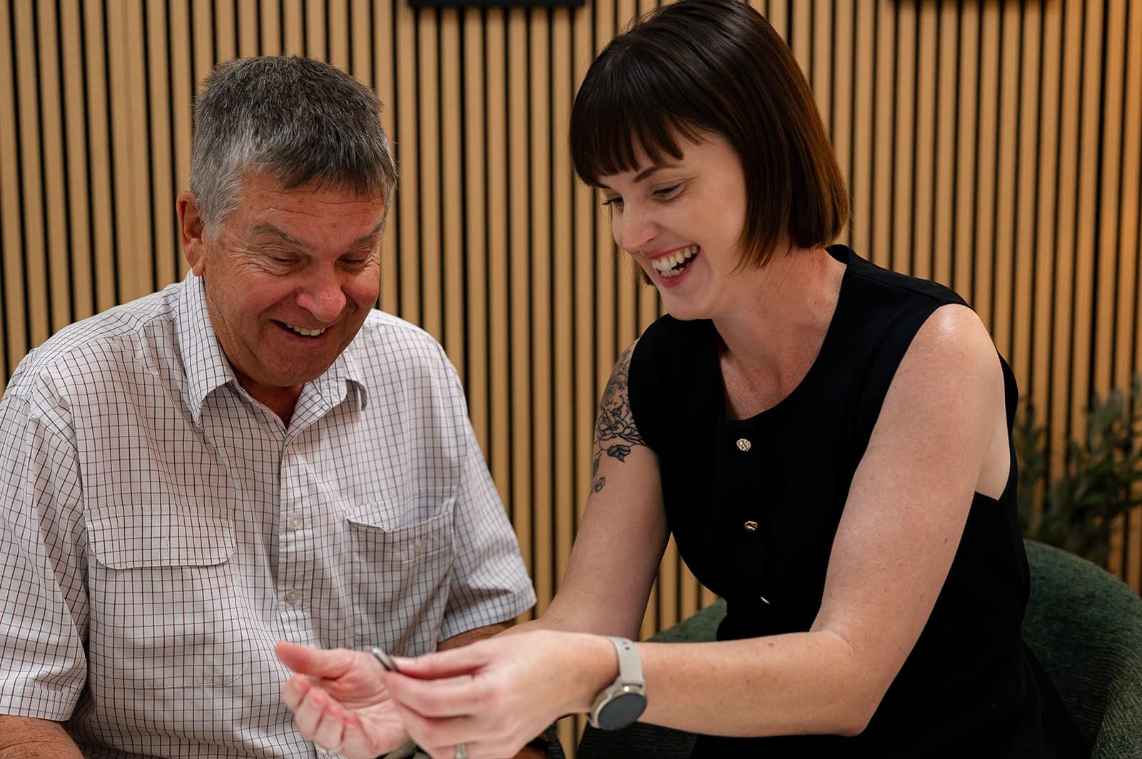 Dr Alison Collins showing a hearing aid in her open palm to a smiling older man