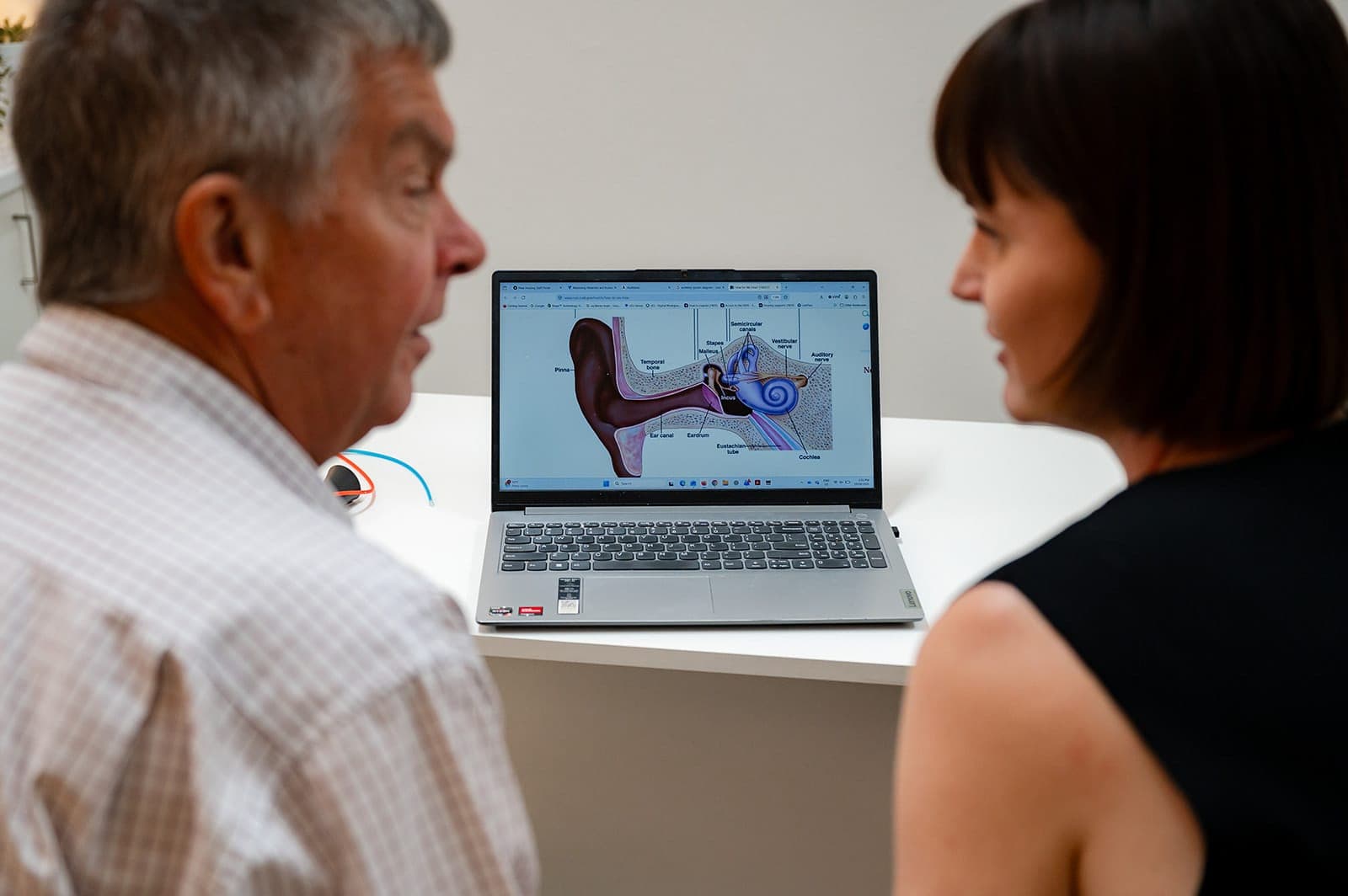 Dr Alison Collins and an older man looking at an ear anatomy diagram on a laptop